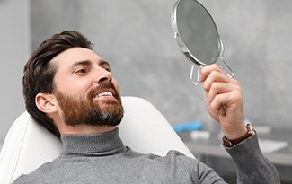 Man smiling in the mirror at the dentist’s office